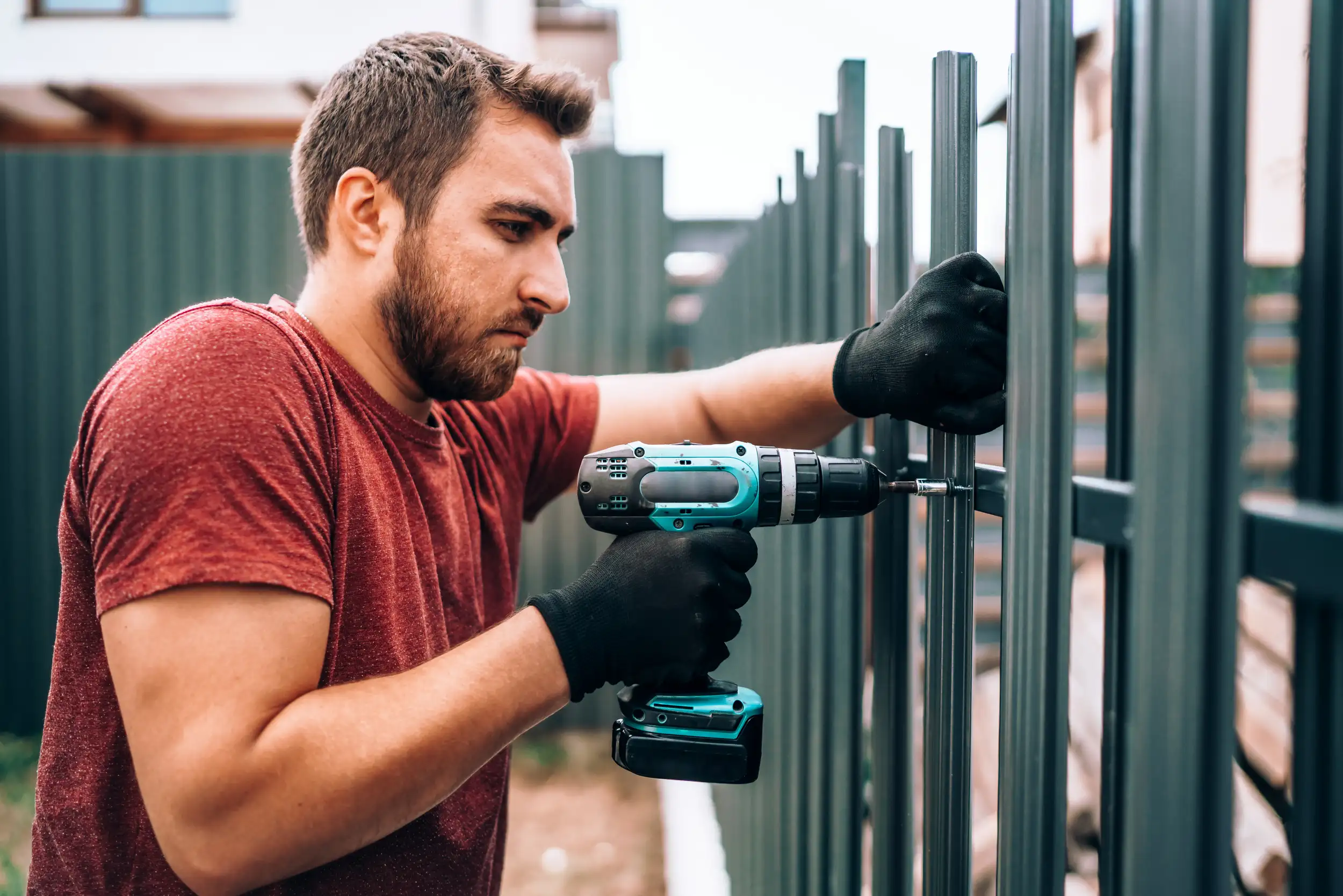 A handyman worker is installing a metal fence with driller.